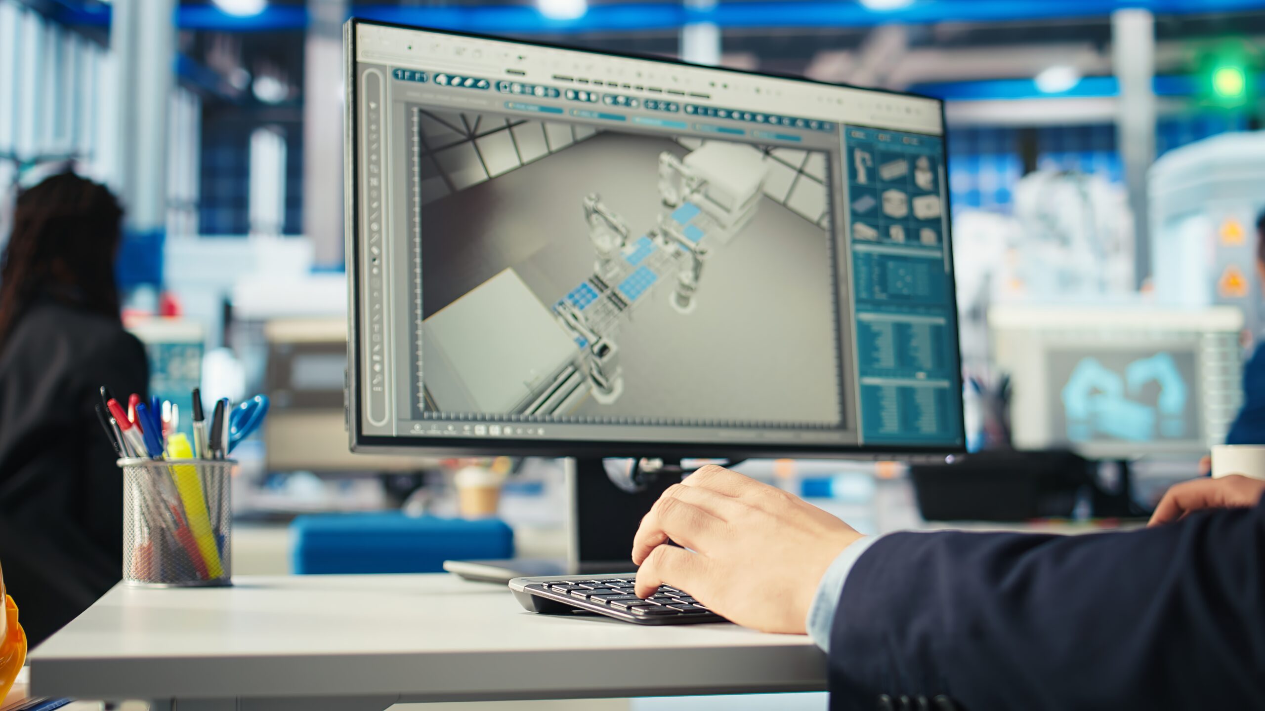 Engineer working on a computer with CAD software displaying a 3D model of industrial machinery.